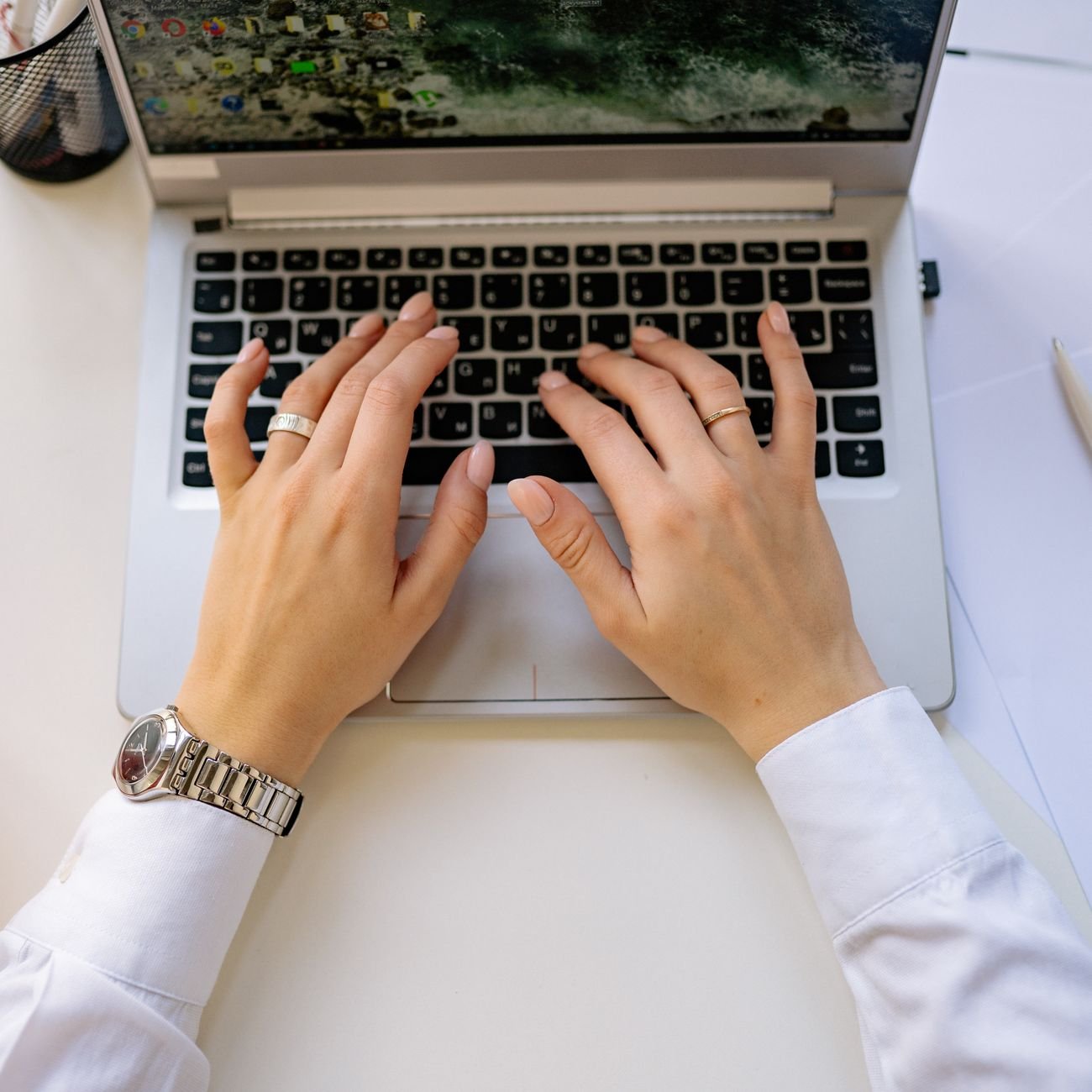 Hands typing on a sleek laptop keyboard in a bright, modern workspace.